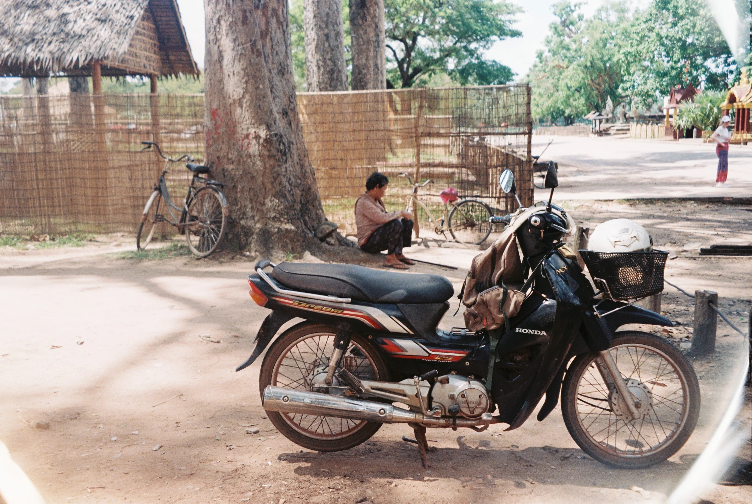 A man sitting on a motorbike in the shade in Thailand.