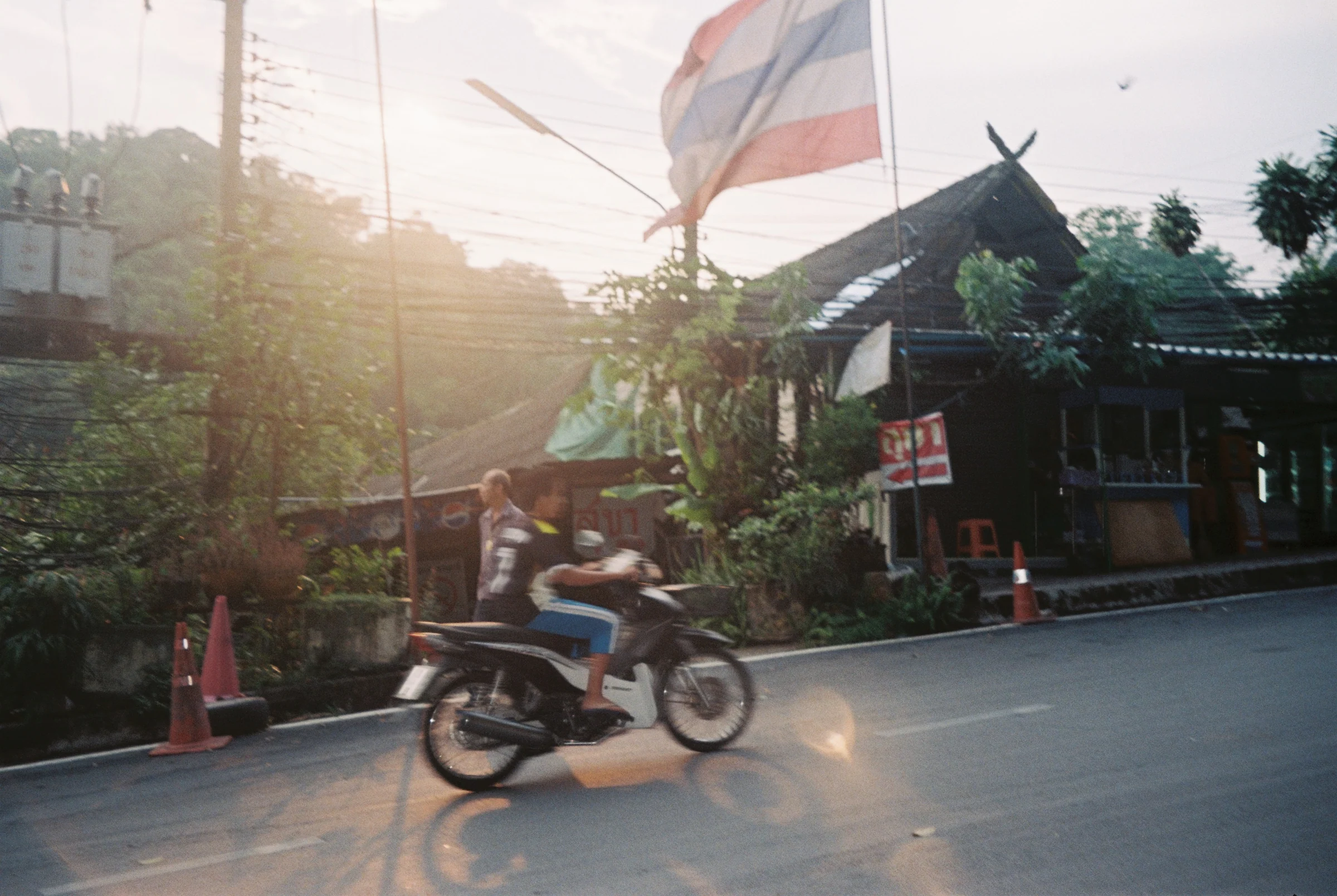 A motorbike passing a Thai flag in warm afternoon light.